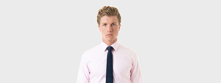 man wearing pink shirt with navy tie on a gray background