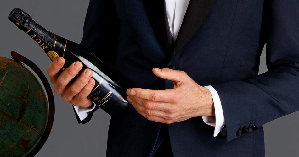 crop of a man's hands wearing a tuxedo and holding a champagne bottle