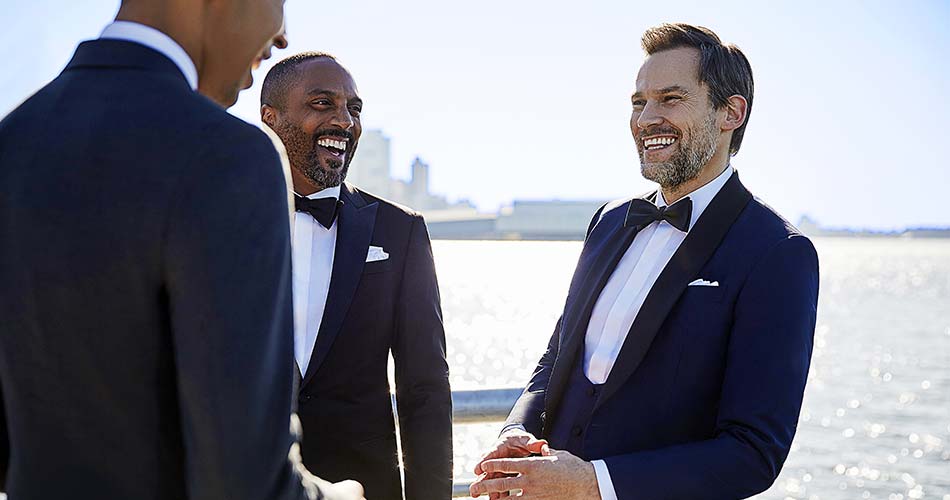 three men wearing blue tuxedo laughing against river backdrop