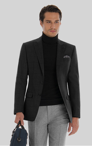 man wearing black turtleneck with dark gray blazer and gray pants holding a bag