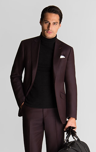 man wearing black turtleneck with burgundy suit holding a bag