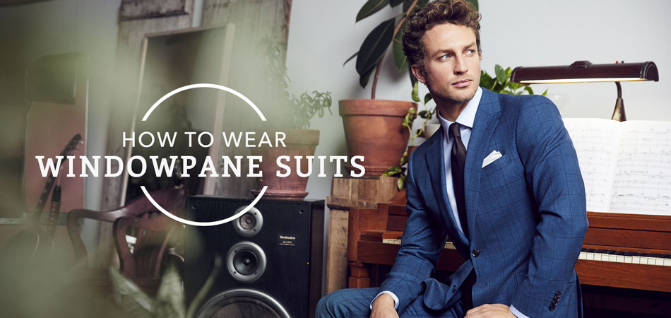 man wearing blue windowpane suit sitting down in front of a piano with text overlay reading 'how to wear windowpane suits'