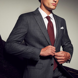 man buttoning dark charcoal suit with white shirt and burgundy tie