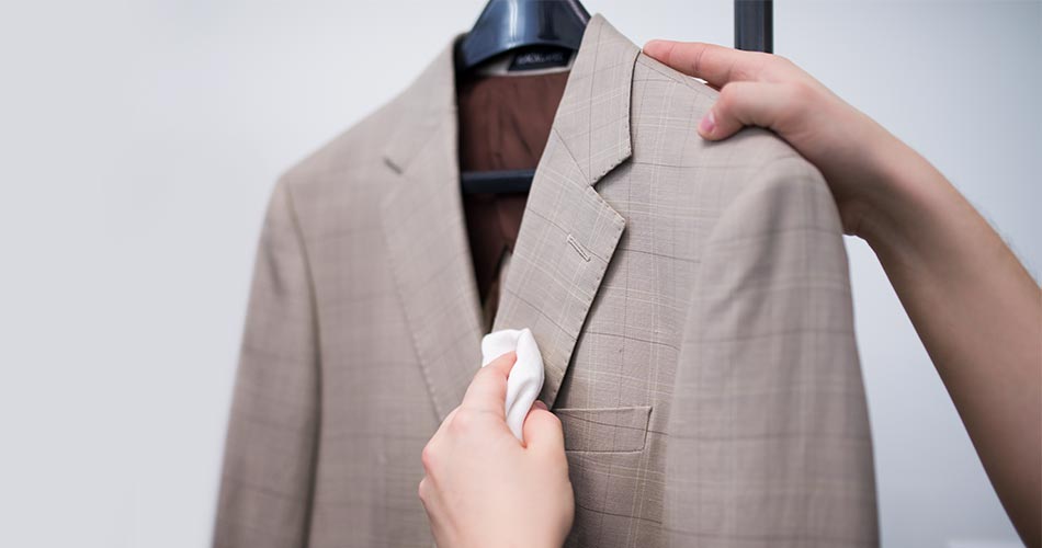 man holding a tan suit blazer while dabbing the front lapel with a white towel