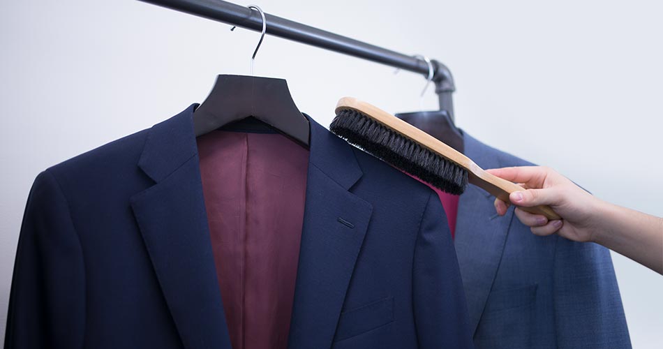 a man's hand holding a suit brush on the shoulder of a navy blazer