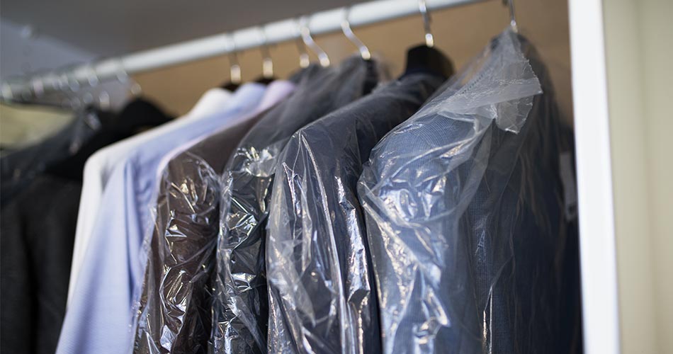 suits in plastic bags and dress shirts hanging in a closet