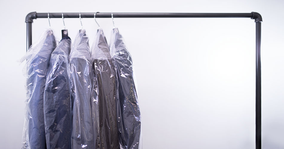 five suits in plastic bigs hanging on a metal rack