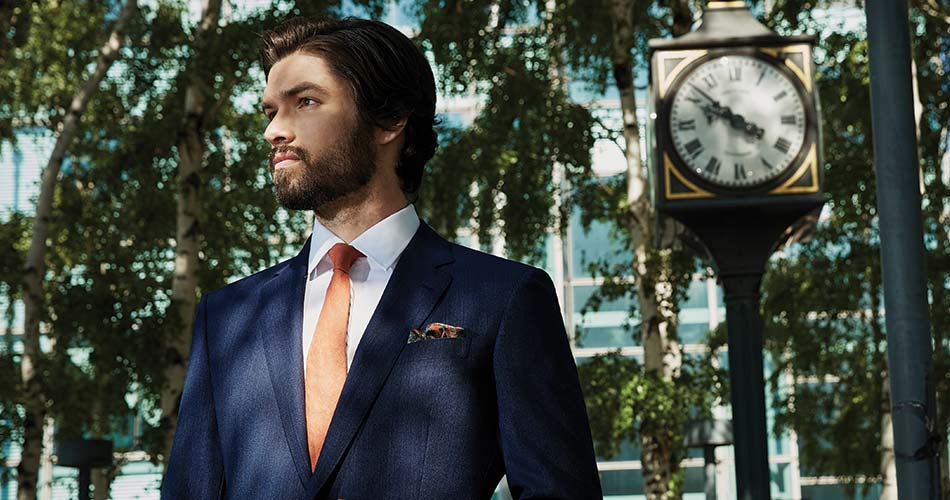 man wearing navy suit and coral tie standing outdoors with a clock tower in the background