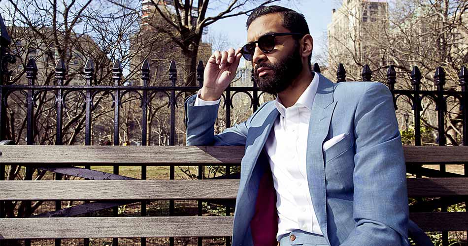 man sitting on a park bench wearing shades, white dress shirt, and linen blazer