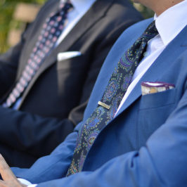 crop of two men wearing suits sitting with focus to a tie clip on a floral blue tie