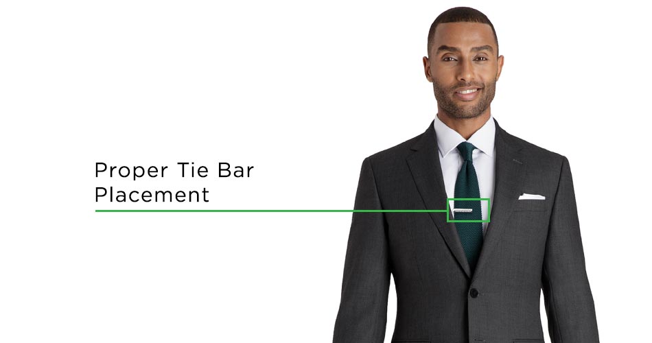 man wearing gray suit with green tie and silver tie clip with the tie clip highlighted with a green box labelled proper tie bar placement