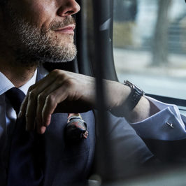 man staring out a car window wearing suit and accessories like cufflinks, a watch, a tie, and pocket square