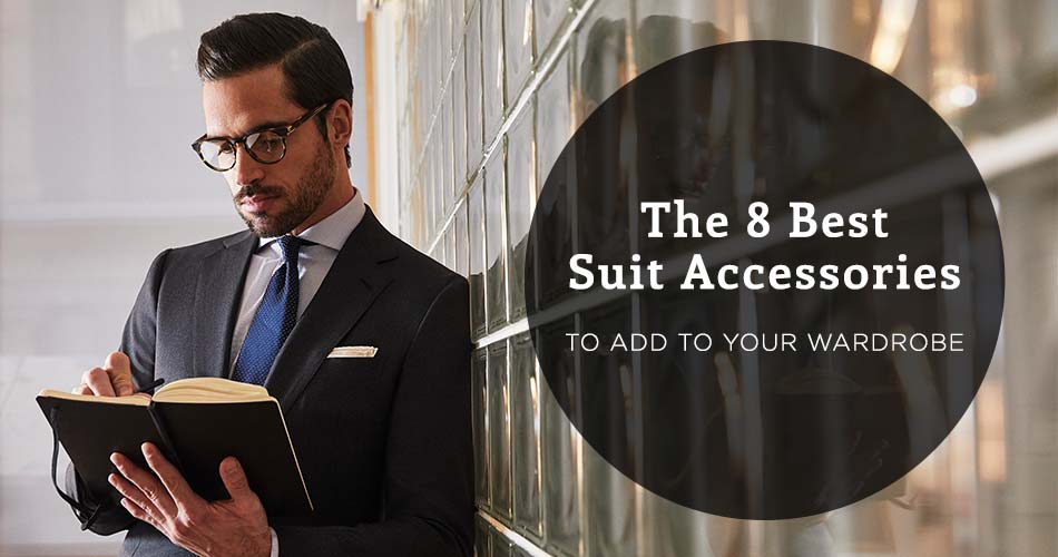 man wearing suit with blue tie with suit accessories pocket square and glasses holding a notebook and leaning against a glass panel wall