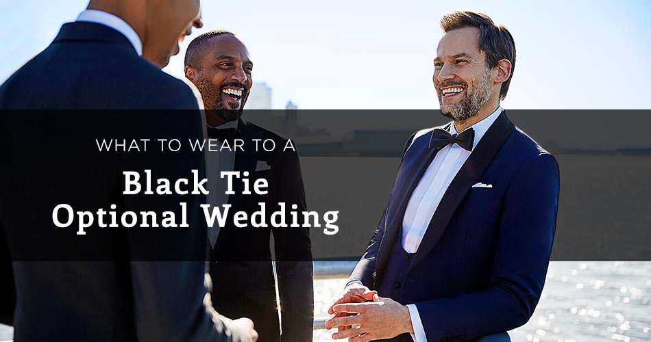 man wearing a marine blue tux on waterfront background with text overlay "what to wear to a black tie optional wedding"