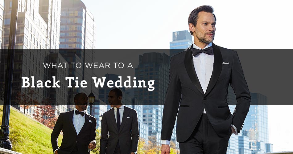 man wearing black tux and black bowtie in the city with text overlay "what to wear to a black tie wedding"
