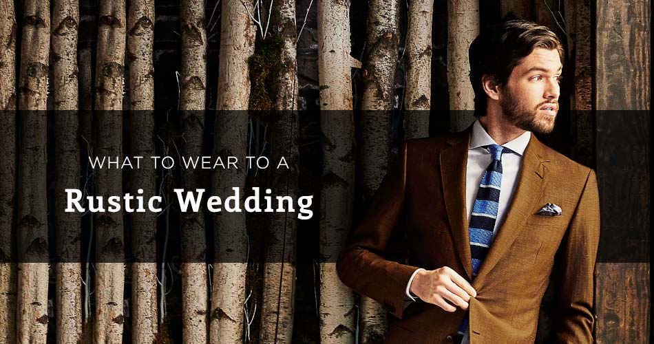 man wearing a brown suit leaning against a rustic wooden wall with text overlay "what to wear to a rustic wedding"